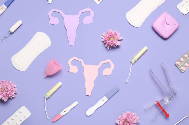 Papiergebärmutter mit gynäkologischem Spekulum, Menstruationspolstern und Schwangerschaftstests auf violettem Hintergrund - Foto, Bild