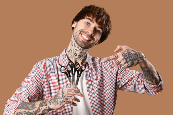 Peluquero tatuado apuntando a tijeras sobre fondo marrón - Foto, Imagen