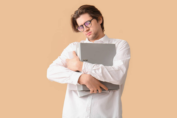 Уставший молодой бизнесмен с ноутбуком на бежевом фоне - Фото, изображение