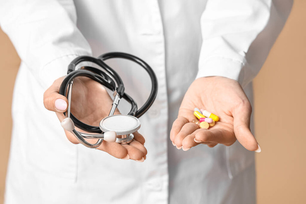 Giovane medico femminile con stetoscopio e pillole su sfondo beige - Foto, immagini