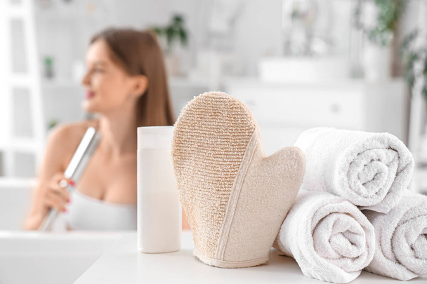 Luva de massagem com toalhas e gel de banho na mesa no banheiro, close-up - Foto, Imagem