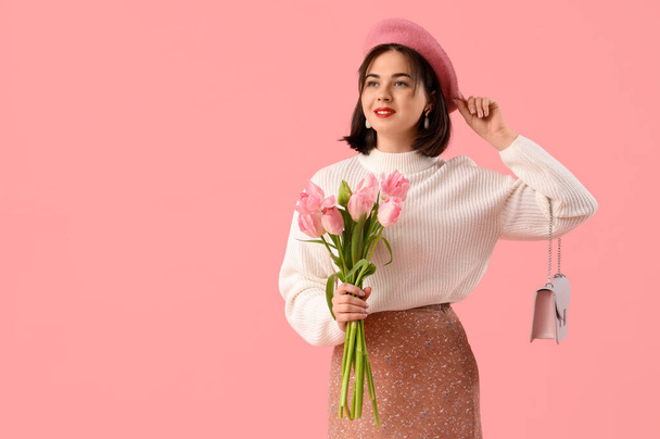 Retrato de mujer joven de moda en boina con flores de tulipán sobre fondo rosa - Foto, imagen