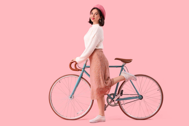 Портрет модної молодої жінки в Береті з велосипедом на рожевому фоні - Фото, зображення