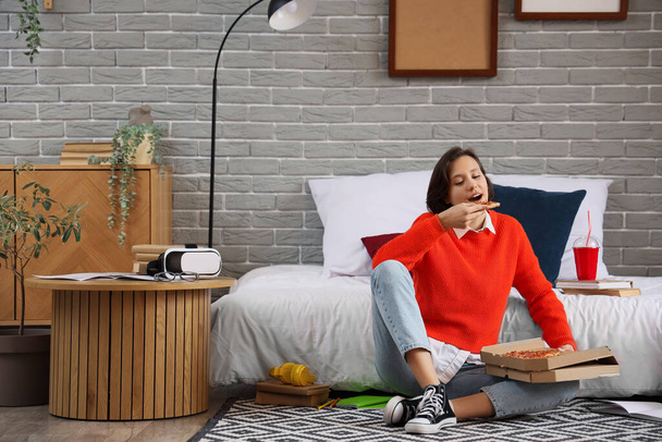 Female student eating tasty pizza in bedroom - Photo, Image