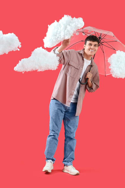 Νεαρός με ομπρέλα και σύννεφα σε κόκκινο φόντο - Φωτογραφία, εικόνα