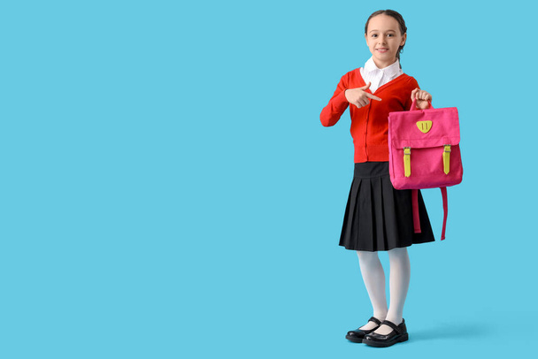 Boldog kis iskolás lány rámutatva hátizsák kék háttér - Fotó, kép