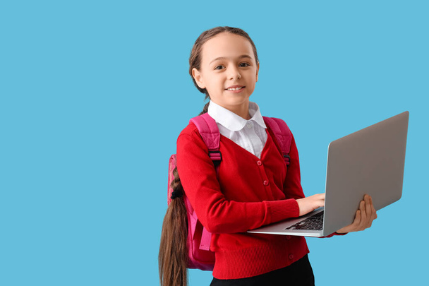 Happy little uczennica z plecakiem i laptopem na niebieskim tle - Zdjęcie, obraz