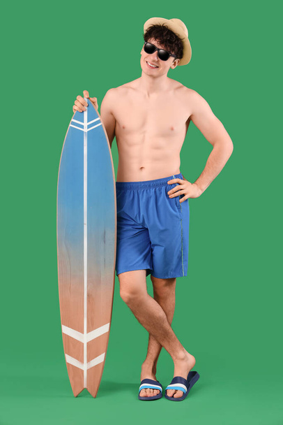 Beau jeune homme heureux avec planche de surf sur fond vert - Photo, image