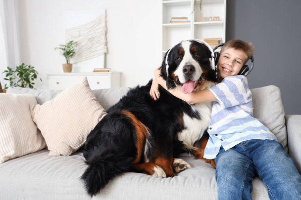 Kleiner Junge mit Berner Sennenhund im Kopfhörer sitzt zu Hause auf Sofa - Foto, Bild
