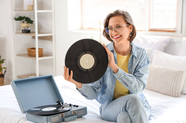 Junge Frau mit Schallplatte und Plattenspieler im Schlafzimmer - Foto, Bild