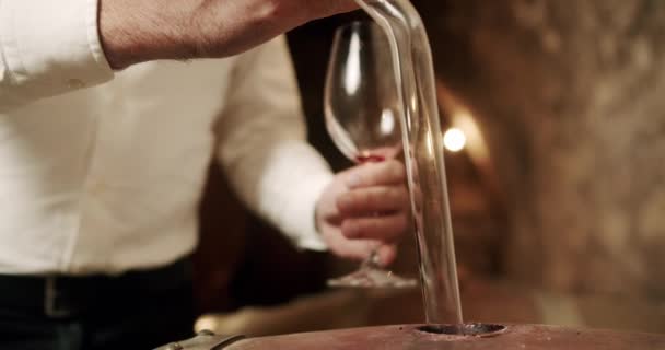 Używając ręki, człowiek z wdziękiem wlewa płyn z drewnianej beczki do szklanki, a jego palce delikatnie chwytają zastawę stołową, gdy kciuk kontroluje przepływ. - Materiał filmowy, wideo