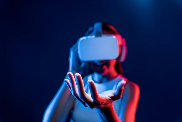 Смарт-жінка, що стоїть в оточенні неонового світла, носить гарнітуру VR, що поєднує метаверсію, футуристичну технологію спільноти кіберпростору. Елегантна жінка використовує ручний об'єкт, що тримає віртуальний об'єкт. галюцинації. - Фото, зображення