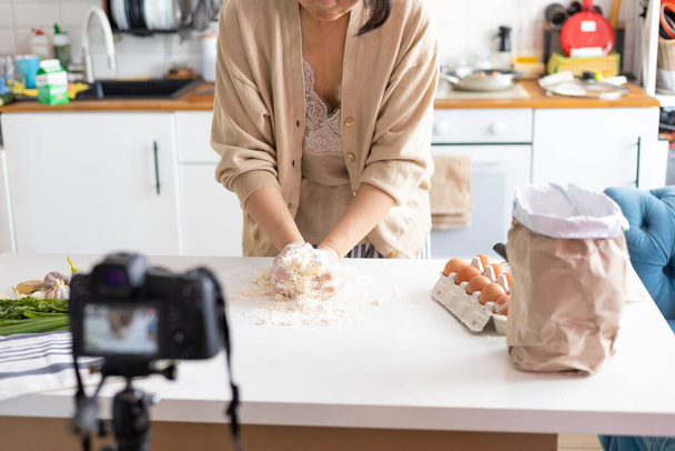 Młoda blogerka robi ciasto i nagrywa filmy dla kanału kulinarnego. Kobieta cukiernik vlogs z kamery wideo zamontowane na statywie w kuchni. - Zdjęcie, obraz