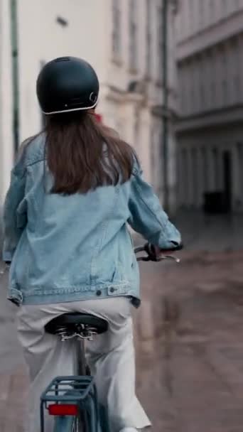 Achteraanzicht van een mooie jonge vrouw op de fiets langs de regenachtige straat in het centrum van de stad. Actieve levensstijl - Video