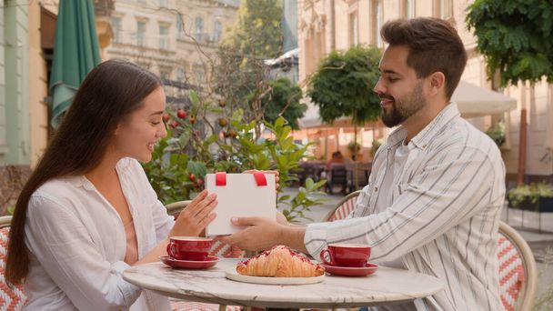 Poikaystävä antaa tyttöystävä lahja odottamaton yllätys vuosipäivä dating miellyttäviä tunteita onnellinen nainen mies hymyilee Valkoihoinen pari kaupunki kahvila ulkopuolella suhde yhdessä rakkaus läsnä paketti romanttinen - Valokuva, kuva