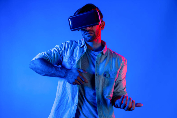 Hombre elegante caucásico con gafas VR y gesto en movimiento sosteniendo la pistola. Gamer utilizando futuros auriculares de realidad virtual digital o innovación futurista para entrar en el mundo meta o jugar juego de acción. Desviación. - Foto, imagen