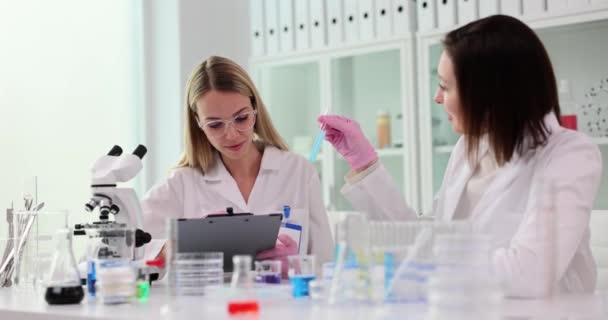 Две женщины-ученые, работающие в лаборатории, довольны результатами, полученными в пробирке, заполненной голубой жидкостью - Кадры, видео