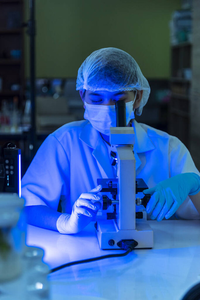 Vertikalwissenschaftlerinnen im Labor betrachten ein wissenschaftliches Mikroskop medizinischer Test zur Erforschung der Biologie Chemie mit blauem hellschwarzem Hintergrund. Männliche Techniker Labor analysieren Chemie Medizinische Forschung - Foto, Bild