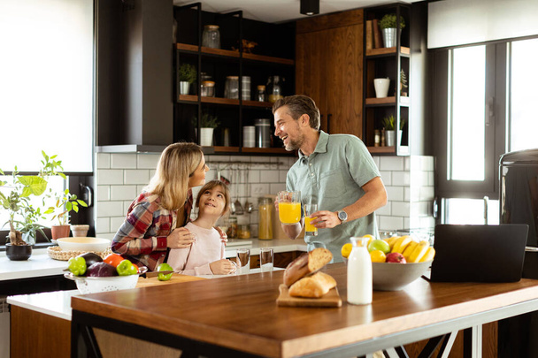 Jeune famille bavardant et préparant la nourriture autour d'un comptoir de cuisine animé rempli d'ingrédients frais et d'ustensiles de cuisine - Photo, image