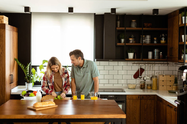 Una pareja feliz disfruta de una conversación informal con bebidas de la mañana en su cocina soleada. - Foto, imagen