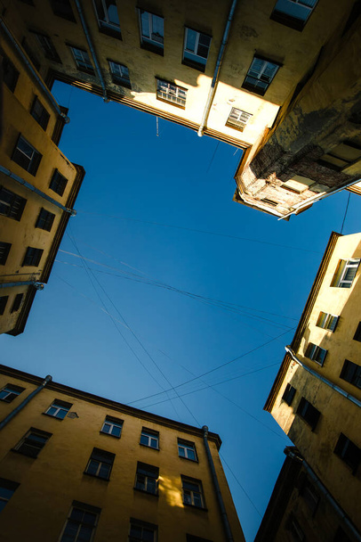 Una escena tranquila capturada en un pozo del patio de San Petersburgo. El cielo azul profundo contrasta con los edificios circundantes, creando una vista pintoresca. - Foto, imagen
