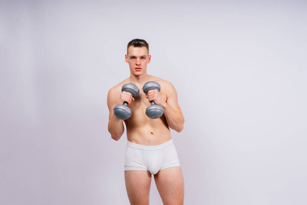 Férfi felpumpált test súlyzókkal a kezében fehér bugyi gyakorlat - Fotó, kép
