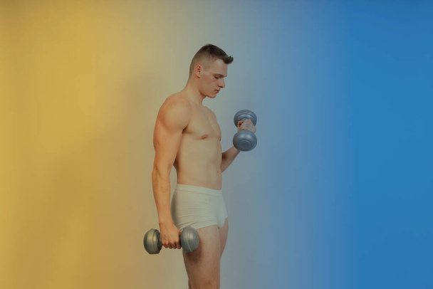 Man with pumped-up body with dumbbells in his hands white panties exercise - Φωτογραφία, εικόνα