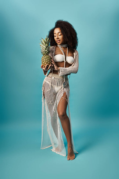 Afroamerykanka w białym bikini trzyma ananasa. - Zdjęcie, obraz