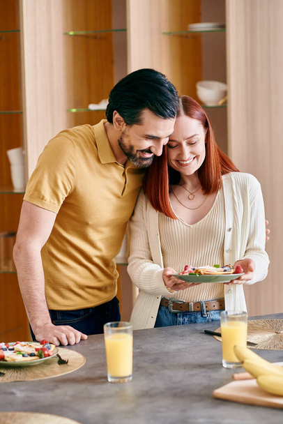 Een roodharige vrouw en een man met baard staan samen in een moderne keuken, genietend van kwaliteitstijd thuis. - Foto, afbeelding