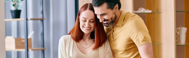 Parrakas mies ja punapää nainen halaavat hellästi modernissa olohuoneessa, ilmaisevat kiintymystä ja läheisyyttä.. - Valokuva, kuva
