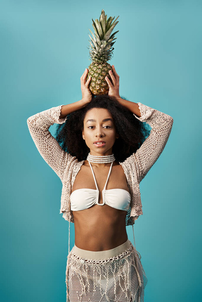 スタイリッシュな水着の若いアフリカ系アメリカ人女性 頭にパイナップルのバランスをとる. - 写真・画像