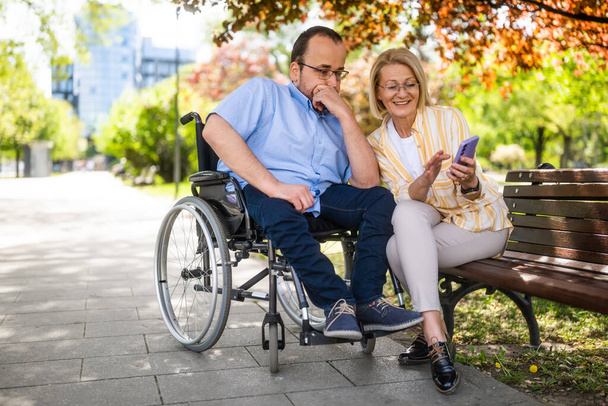 Mężczyzna na wózku inwalidzkim spędza czas z matką w parku. - Zdjęcie, obraz