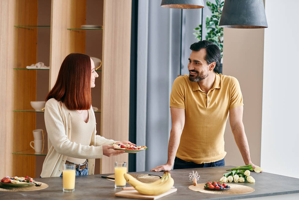 A vörös hajú nő és szakállas férfi áll a modern konyha pult, élvezi a minőségi időt együtt. - Fotó, kép