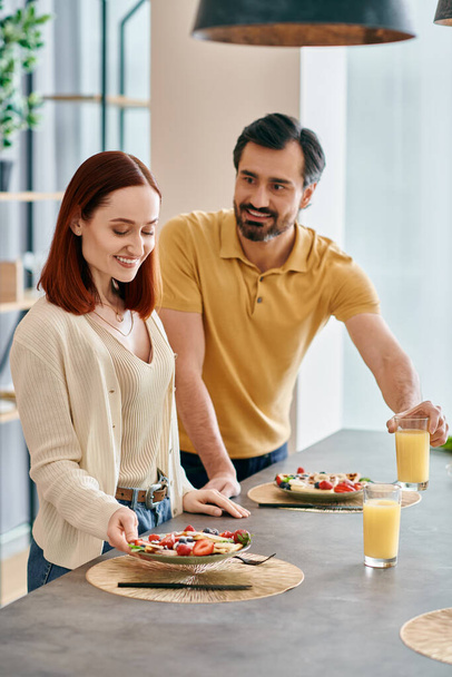 Güzel bir yetişkin çift, kızıl saçlı bir kadın, ve sakallı bir adam, modern bir mutfakta yemek hazırlıyor, evde birlikte güzel vakit geçiriyorlar.. - Fotoğraf, Görsel
