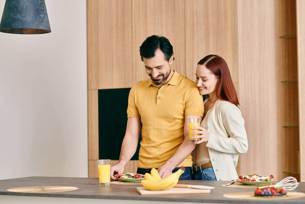 Una hermosa pareja de adultos, una mujer pelirroja y un hombre barbudo, preparando el desayuno en un apartamento moderno. - Foto, imagen