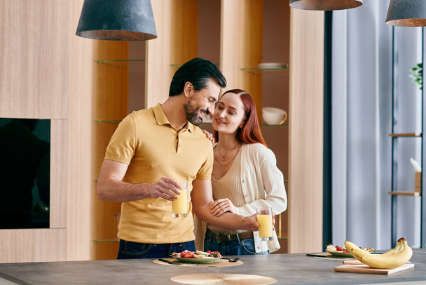 Una rossa e un uomo barbuto condividono un momento accogliente, in piedi insieme in una cucina moderna. - Foto, immagini
