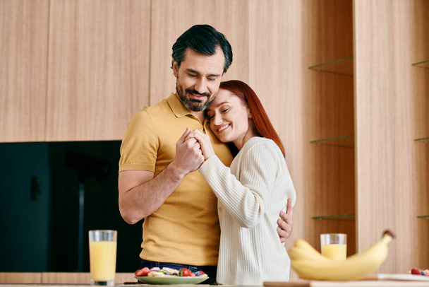 Rudowłosa kobieta i brodaty mężczyzna namiętnie objąć w nowoczesnej kuchni, pokazując miłość i wspólnotę. - Zdjęcie, obraz