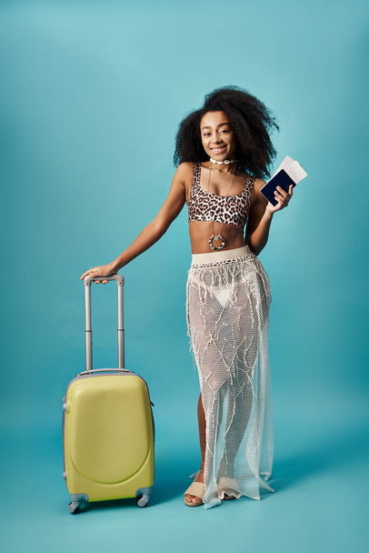 Молодая женщина с чемоданом и паспортом позирует на синем фоне - Фото, изображение