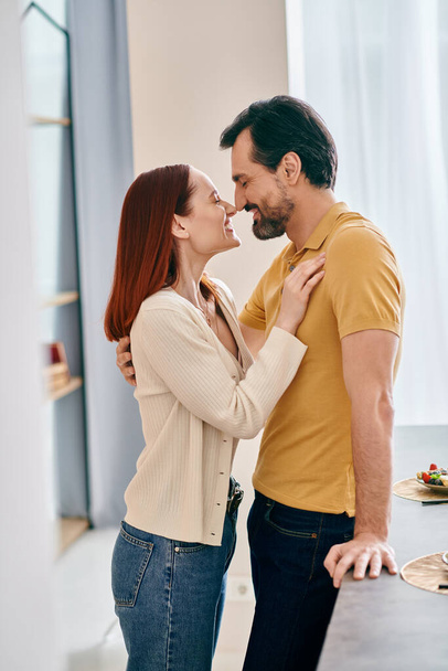 現代のキッチンで情熱的なキスを共有する赤毛の女性とひげ付き男性,愛とつながりを表現. - 写真・画像