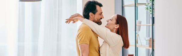 Руда жінка і бородатий чоловік поділяють теплі обійми в затишній вітальні, створюючи прекрасний момент близькості і зв'язку. - Фото, зображення