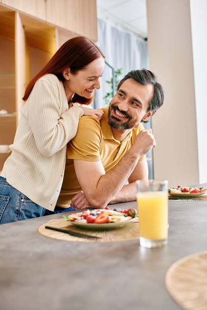 Ein bärtiger Mann und eine rothaarige Frau frühstücken fröhlich zusammen in ihrer modernen Küche. - Foto, Bild