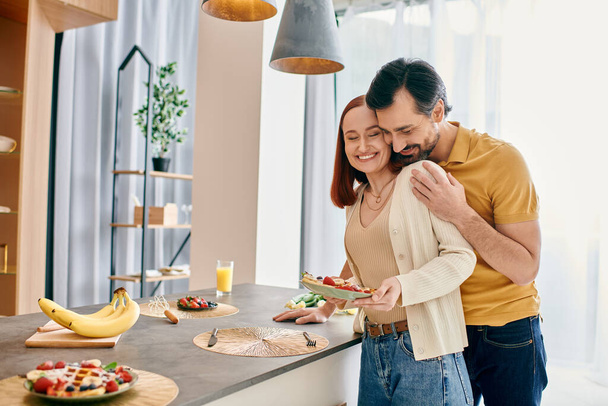 Ένας γενειοφόρος άνδρας και μια κοκκινομάλλα απολαμβάνουν ένα ζεστό πρωινό μαζί σε μια σύγχρονη κουζίνα διαμέρισμα. - Φωτογραφία, εικόνα