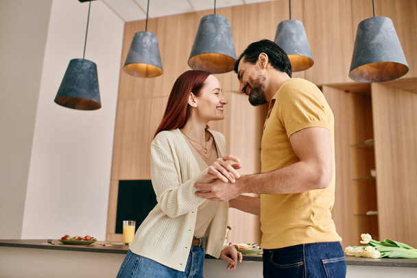 Красивая взрослая пара, рыжая женщина и бородатый мужчина, стоя вместе на современной кухне, проводя время. - Фото, изображение