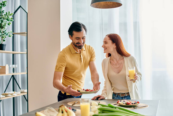 赤毛の女性と髭の男は,モダンなキッチンで一緒に朝食を楽しんでいます. - 写真・画像