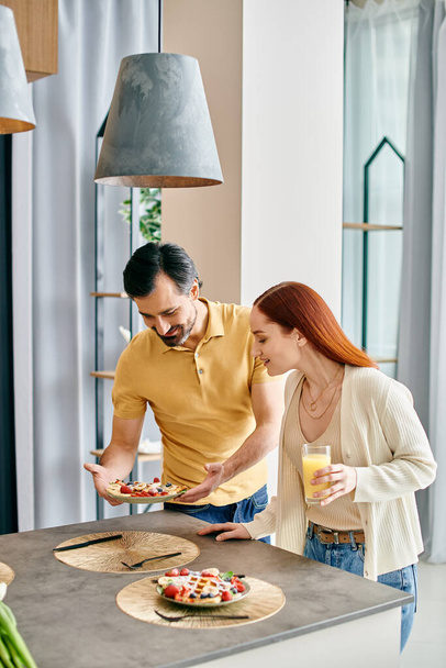 Una donna rossa e un uomo barbuto che si godono un pasto insieme in una moderna cucina appartamento. - Foto, immagini