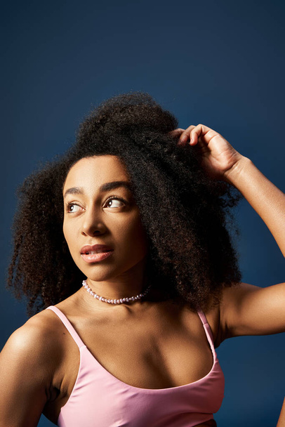 Eine stylische junge Afroamerikanerin mit lockiger Frisur posiert vor blauem Hintergrund. - Foto, Bild