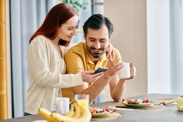Rudowłosa kobieta i brodaty mężczyzna koncentrują się na telefonach podczas śniadania w nowoczesnym mieszkaniu. - Zdjęcie, obraz