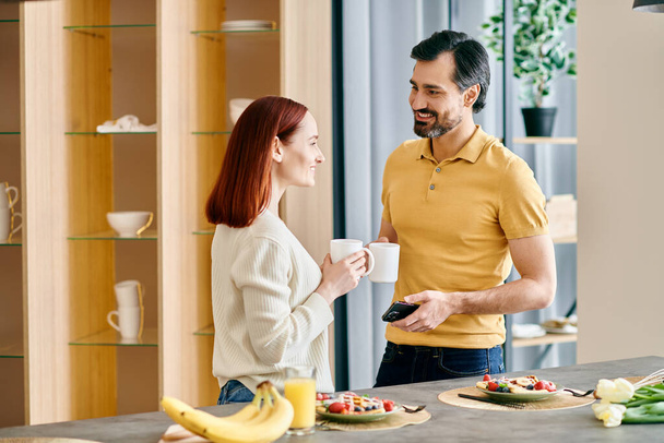 Μια όμορφη κοκκινομάλλα γυναίκα και ένας γενειοφόρος άντρας που συμμετέχουν σε μια εγκάρδια συζήτηση σε μια σύγχρονη κουζίνα. - Φωτογραφία, εικόνα