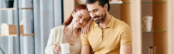 Egy gyönyörű felnőtt pár, egy vörös hajú nő és egy szakállas férfi, együtt ülnek egy asztalnál egy modern lakásban, minőségi időt töltve. - Fotó, kép