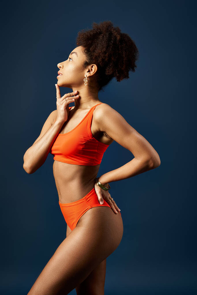 Elegante mujer afroamericana en bikini naranja posando sobre fondo azul. - Foto, Imagen